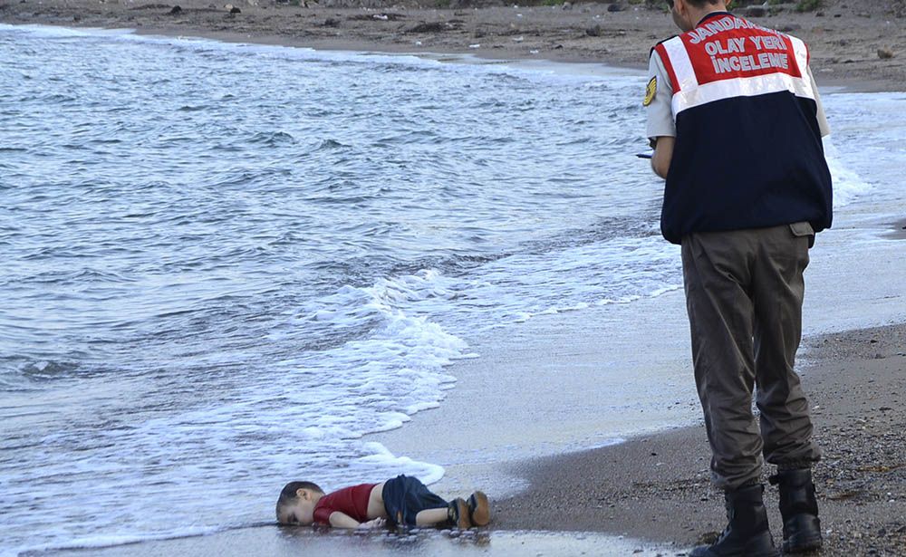TOPSHOTS GRAPHIC CONTENT A Turkish police officer stands next to a migrant child's dead body off the shores in Bodrum, southern Turkey, on September 2, 2015 after a boat carrying refugees sank while reaching the Greek island of Kos. Thousands of refugees and migrants arrived in Athens on September 2, as Greek ministers held talks on the crisis, with Europe struggling to cope with the huge influx fleeing war and repression in the Middle East and Africa. AFP PHOTO / DOGAN NEWS AGENCY = TURKEY OUT =